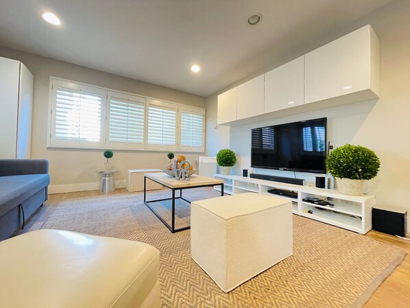 A modern living room with a flat-screen TV, white cabinetry, and a grey sofa.
