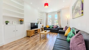 Ein modernes Wohnzimmer mit einer schwarzen Couch, einem Holztisch, weißen Schränken und einem Fernseher.