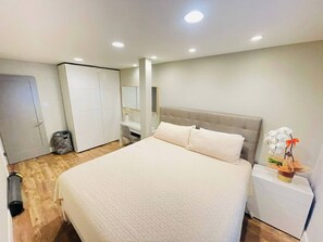 A bedroom with a bed, a bedside table, a wardrobe, and a trash bin.