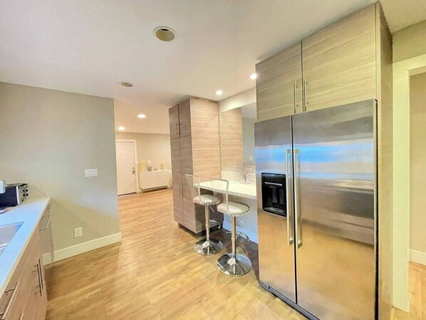 A modern kitchen with a stainless steel refrigerator, wooden cabinets, and a bar area with stools.