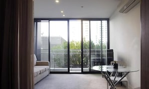 Una habitación moderna con sofá, una mesita y vistas a edificios y árboles a través de amplios ventanales.