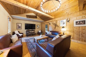 Ein gemütliches Wohnzimmer mit Holzwänden, einem großen Fernseher, Ledersofas und einem gemusterten Teppich.