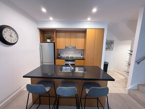 Uma cozinha moderna com ilha central, banquetas, frigorífico e um relógio na parede.