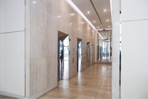 A modern hallway with marble walls and a wooden floor, leading to elevators and a glass door entrance. - Comfortable Studio Stay with Spa & Sauna Access (South Yarra)