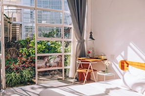A hotel room with a large window, a bed, a small table with a lamp, and a view of greenery outside. - The LOOP Boutique Hotel & Café (Da Lat)