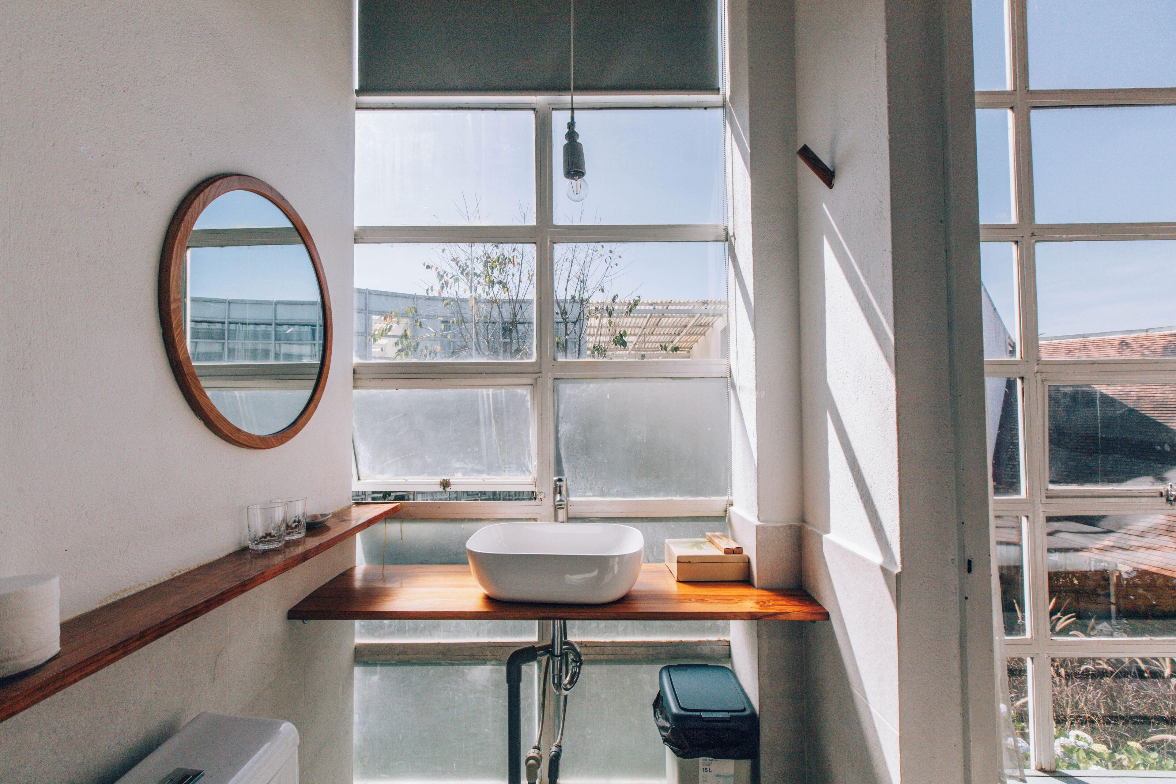 A bathroom with a large window, a round mirror, and a white sink.