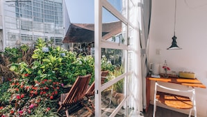Habitación de hotel moderna con pared de vidrio, muebles de madera y vistas a un jardín.