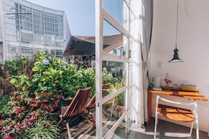 A modern hotel room with a glass wall, wooden furniture, and a view of a garden. - The LOOP Boutique Hotel & Café (Da Lat)
