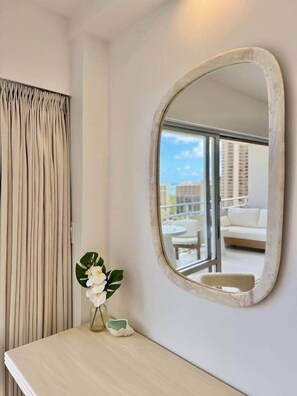 Ein Zimmer mit einem großen, ovalen Spiegel, einem Fenster mit Blick auf einen Balkon und einem kleinen Tisch mit Blumen in einer Vase.