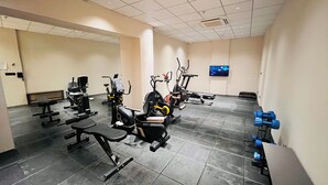 Een sportschool met diverse trainingsapparaten, een televisie en een betegelde vloer.