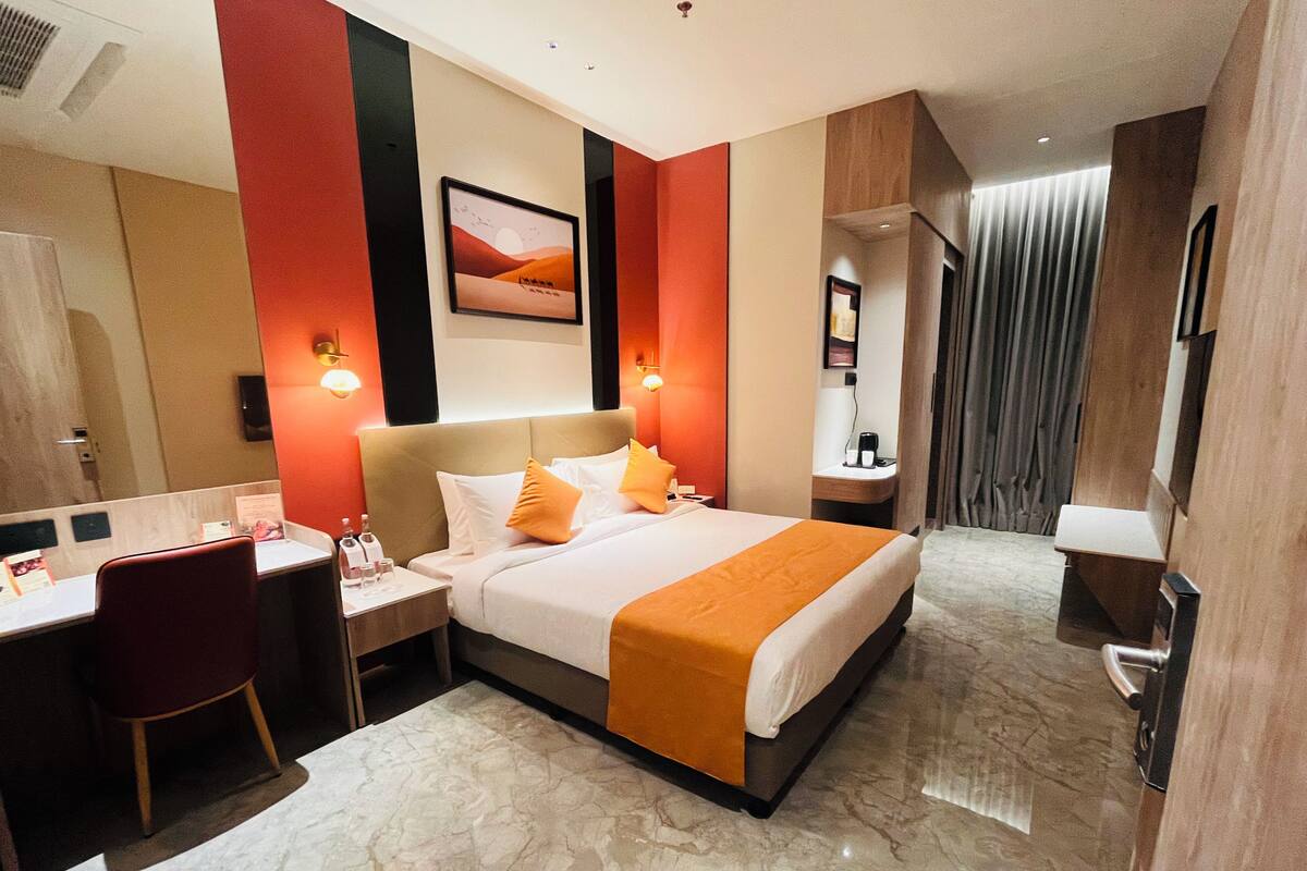 Una habitación de hotel con cama, escritorio, silla y un cuadro en la pared.