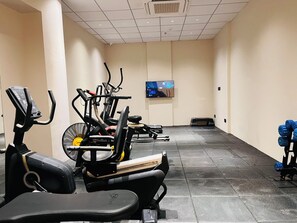 A gym with exercise equipment, a television, and a wall-mounted fan. - Ira By Orchid Bhavnagar (Bhavnagar)