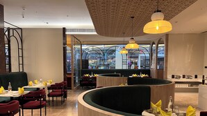 Een restaurant met een gebogen houten receptiebalie, rode gestoffeerde stoelen en gele servetten.