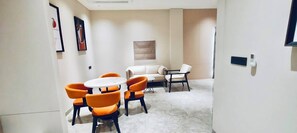A modern room with a round table and orange chairs, a sofa, and a TV mounted on the wall.