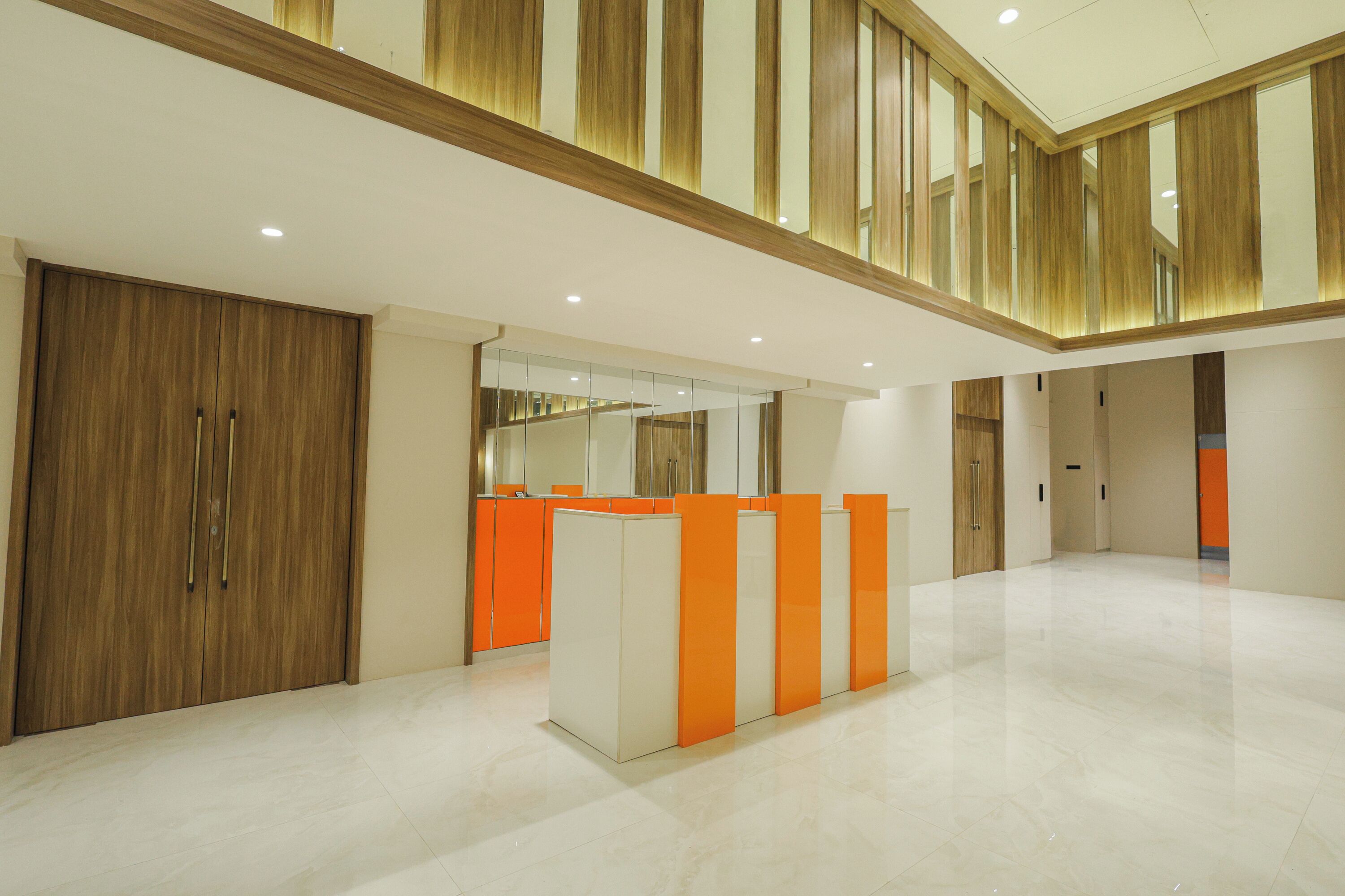 Un vestíbulo amplio con techo alto, paneles de madera y una recepción con detalles en naranja.