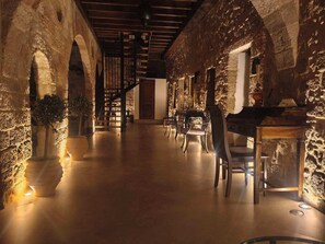 A spacious corridor with stone walls, wooden beams, and a piano.