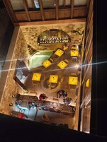 Egy tetőterasz, melynek kőből készült falai vannak, emellett egy medence, valamint sárga színű asztalok és székek találhatók rajta.