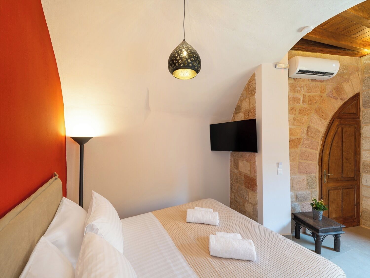 Habitación de hotel con cama, televisor empotrado, aire acondicionado y pared de piedra.