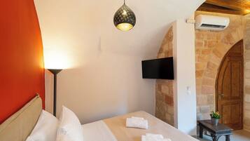 Habitación de hotel con cama, televisor empotrado, aire acondicionado y pared de piedra.