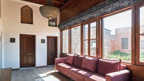 A room with a wooden ceiling, a large window with a view of buildings, a wooden door, and a red sofa. - Jivaeri Luxury Suites (Rhodes)