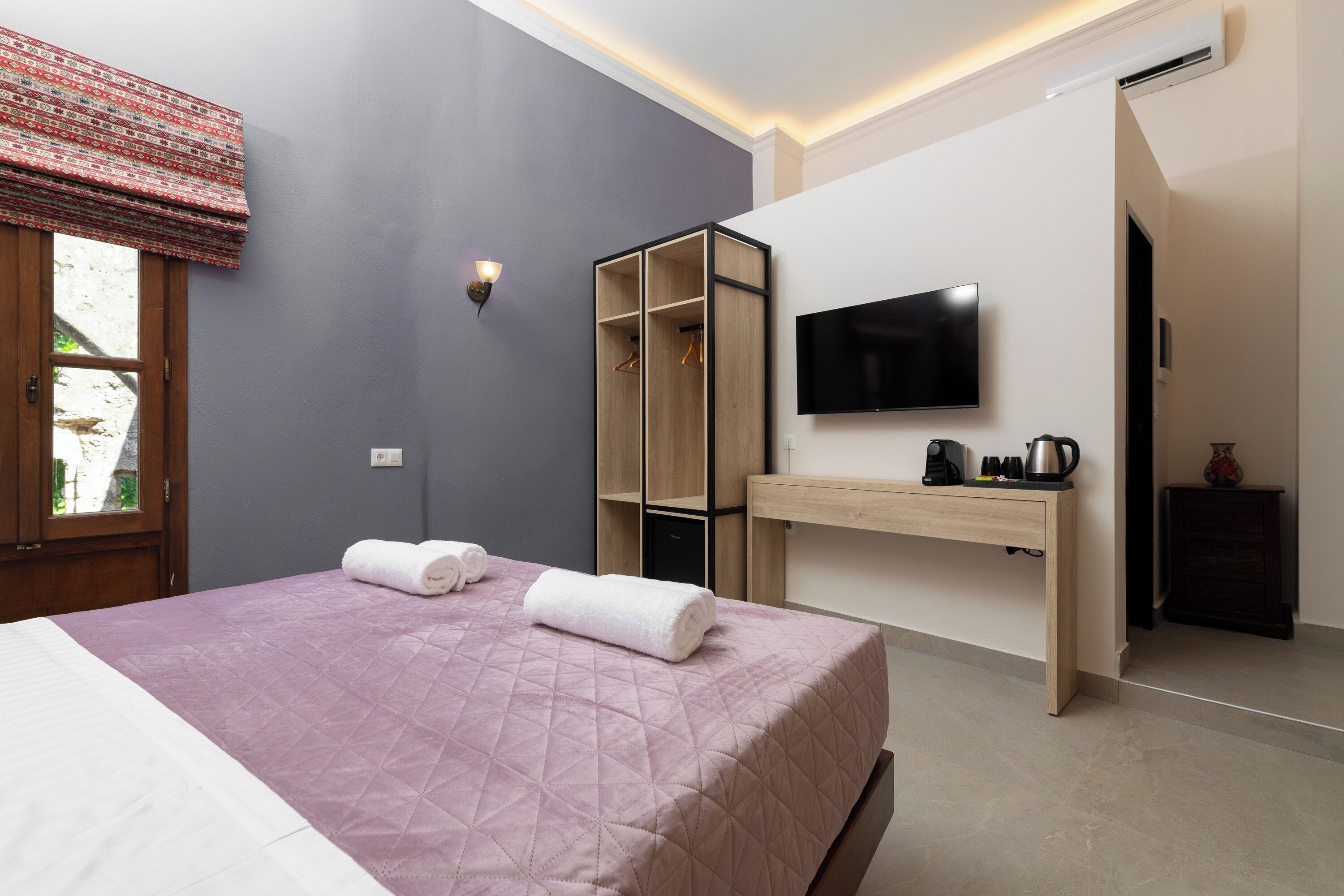 A bedroom with a bed, a TV, a wardrobe, and a desk with a coffee maker.