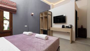 A bedroom with a bed, a TV, a wardrobe, and a desk with a coffee maker.