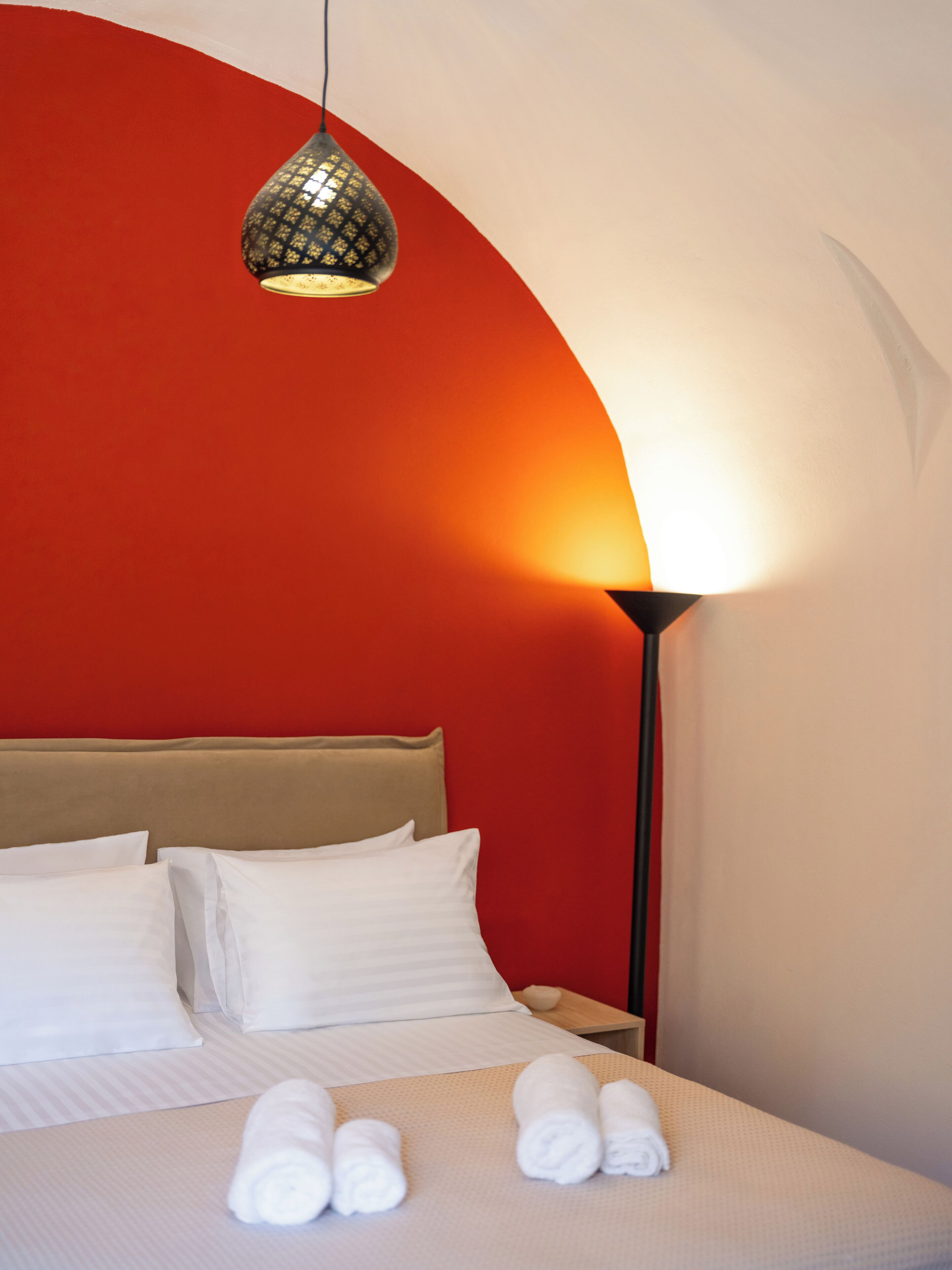 A hotel room with a bed, pillows, a bedside table, a lamp, and rolled towels.