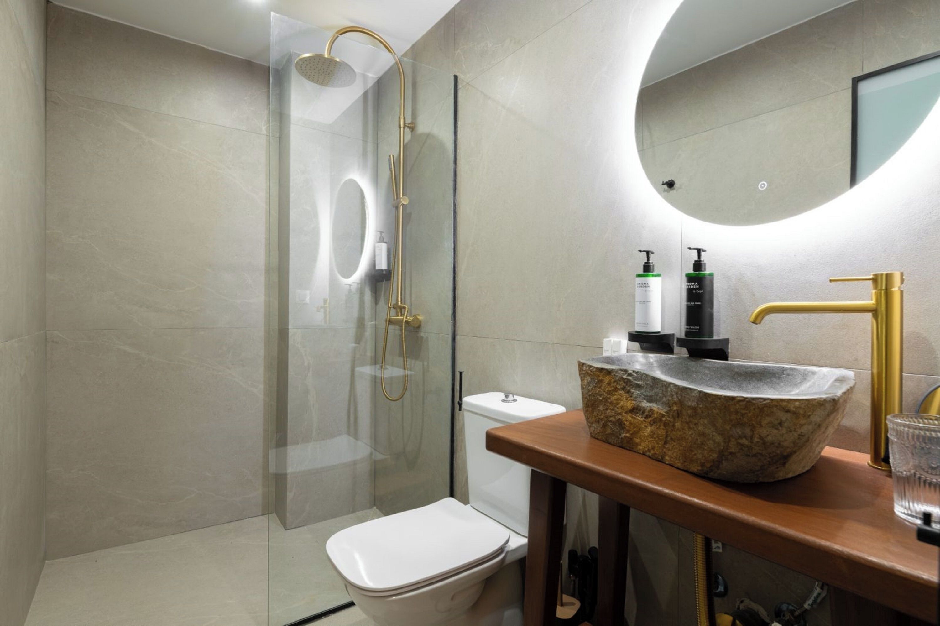 A modern bathroom with a glass-enclosed shower, a white toilet, and a stone sink with a gold faucet.