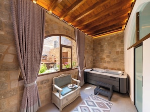 A stone-walled bathroom with a hot tub, a bench, and a window with curtains.