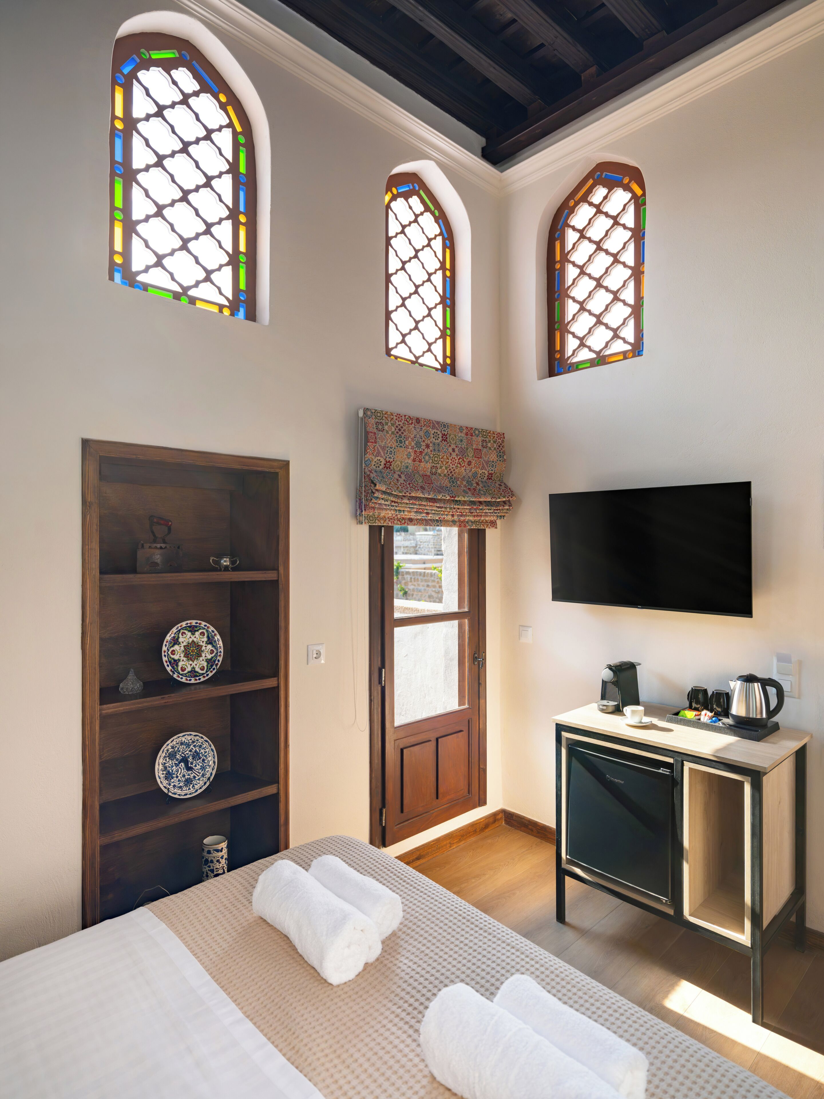 Habitación de hotel con cama, televisión, kitchenette pequeño y tres ventanas de arco.