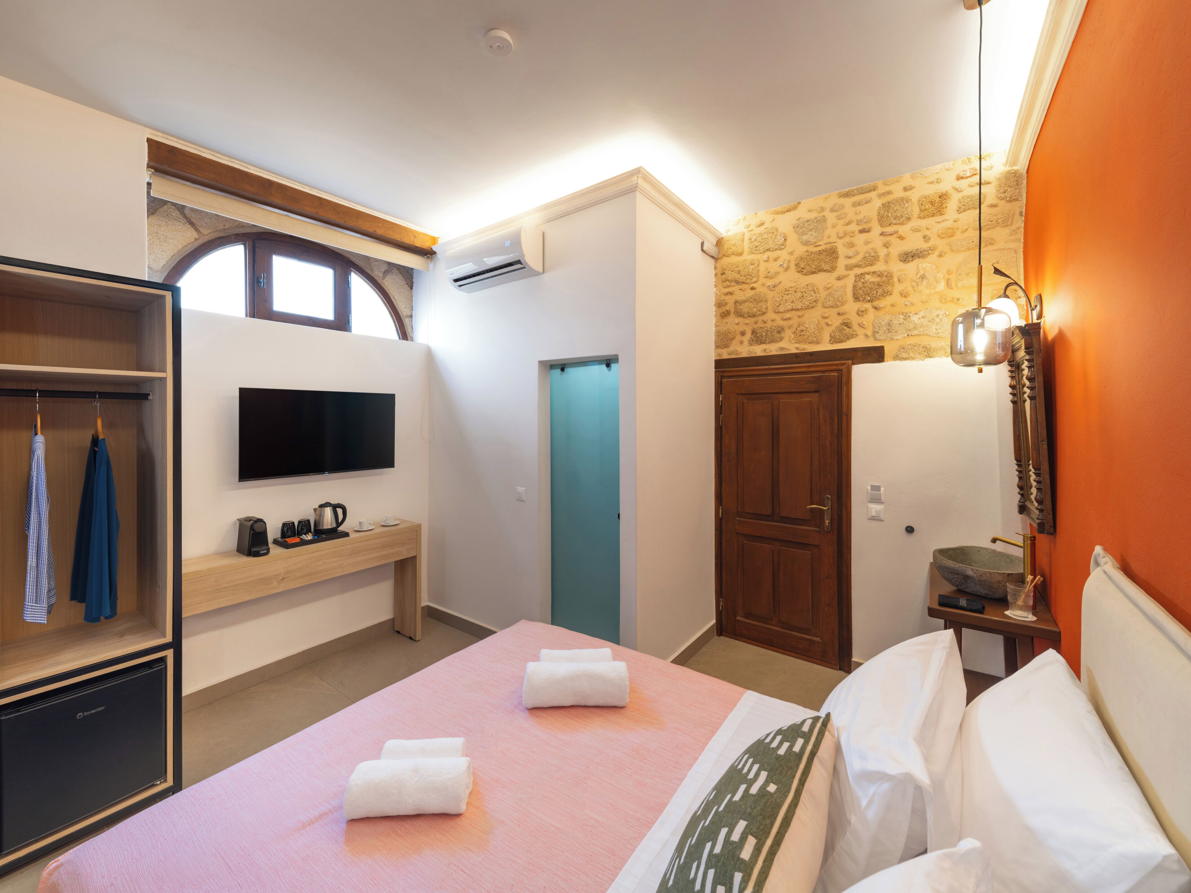 Quarto de hotel com cama, televisão, guarda-roupa, escrivaninha e banheiro.