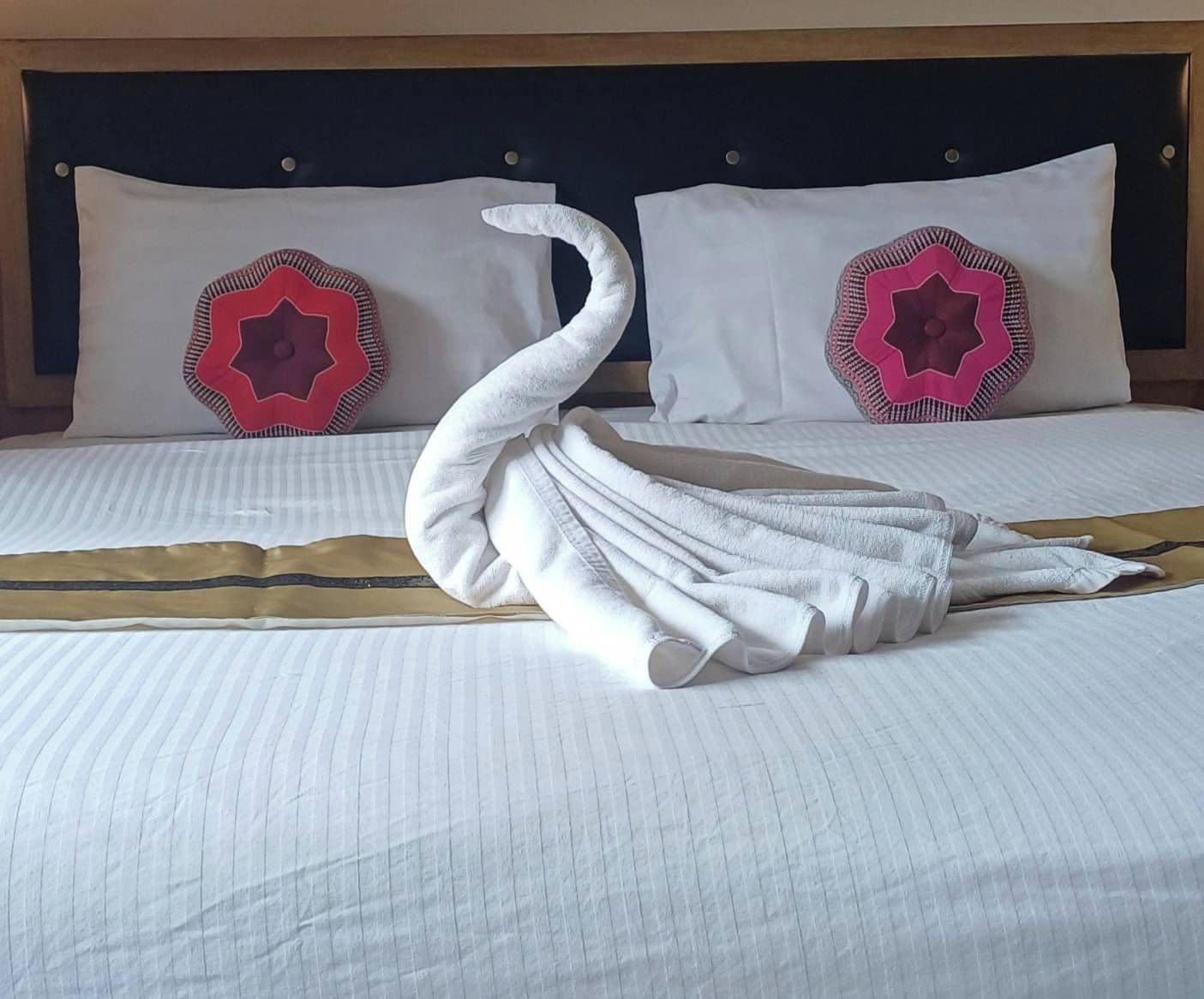 A neatly made bed with a swan-shaped towel arrangement, two pillows with star patterns, and a gold accent pillow.