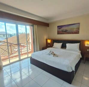 A hotel room with a large bed, a painting on the wall, and a balcony with a view. - Bursa Hotel (Patong)