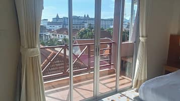 Una habitación con un amplio ventanal corredera que da a un balcón con barandilla roja, una cama con cubrecama blanco y piso de baldosas con diseño.