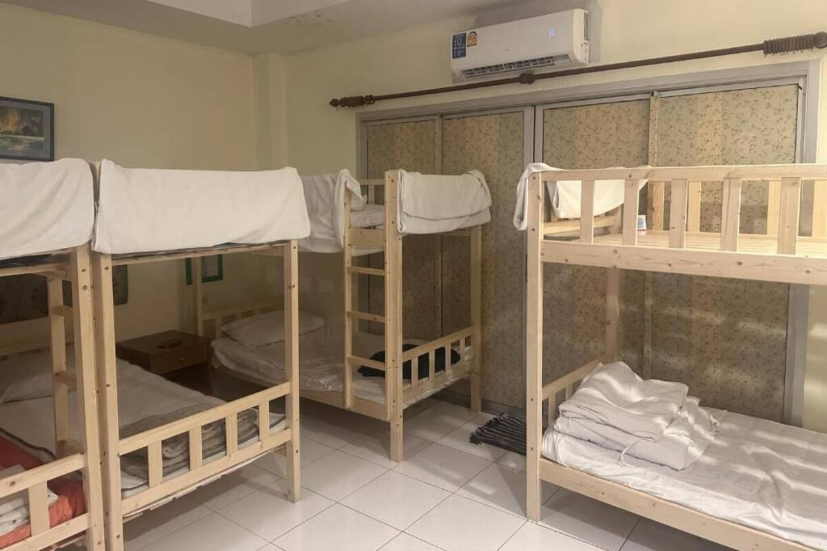 A dormitory room with bunk beds, a wardrobe, and an air conditioning unit.