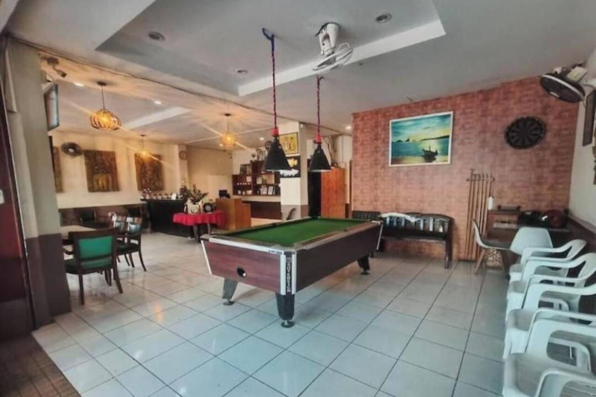 A pool table in a room with a dining area, a bar, and a dartboard on the wall.