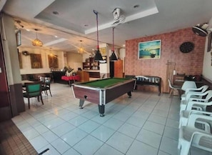 A pool table in a room with a dining area, a bar, and a dartboard on the wall. - Bursa Hotel (Patong)
