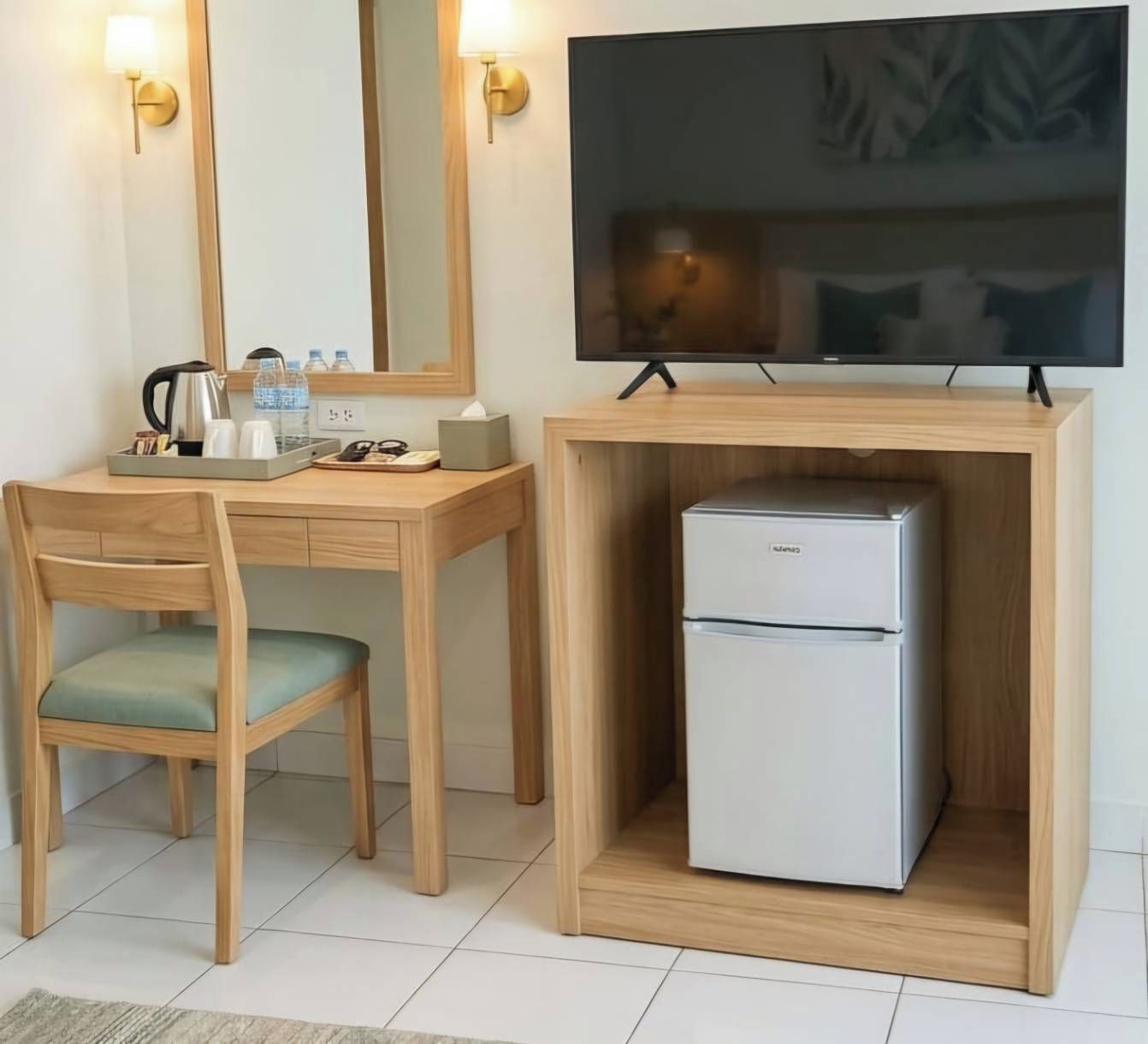 A compact hotel room with a wooden desk, a television, and a mini-fridge.
