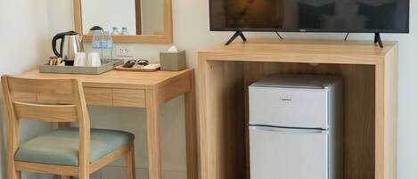 A compact hotel room with a wooden desk, a television, and a mini-fridge.