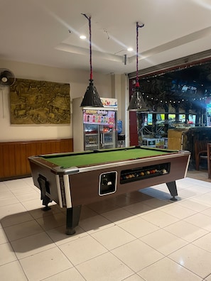 A pool table in a room with a ceiling fan, a wall mural, and a vending machine. - Bursa Hotel (Patong)