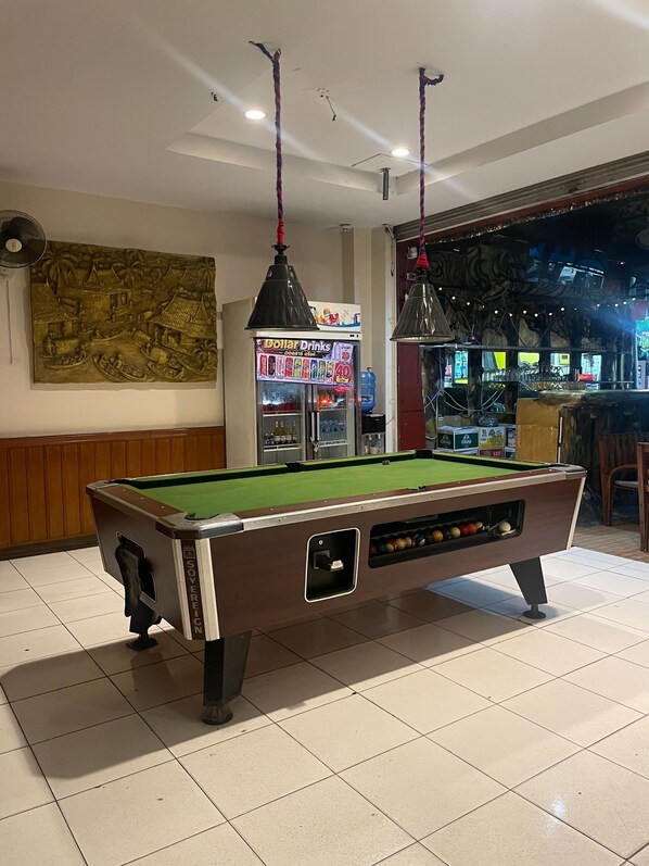 A pool table in a room with a ceiling fan, a wall mural, and a vending machine. - Bursa Hotel (Patong)