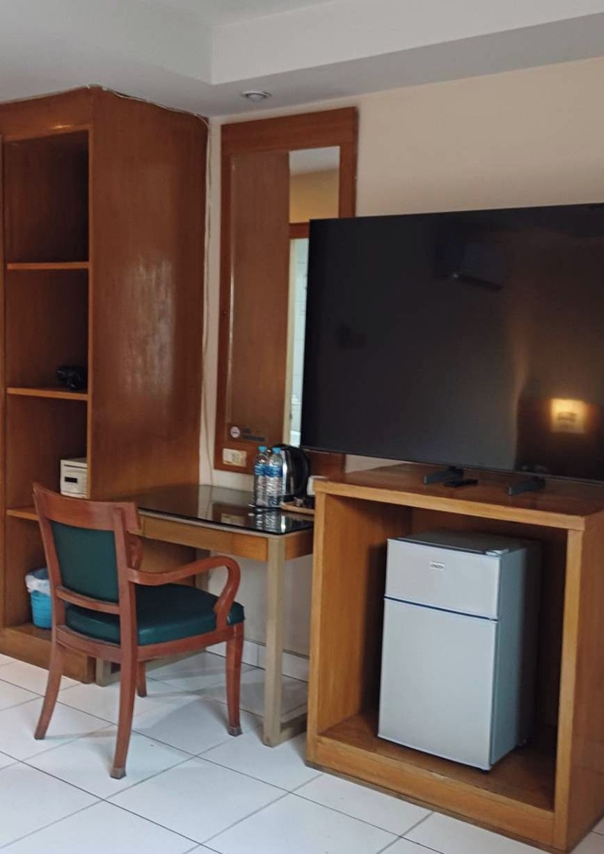 Une chambre équipée d’un bureau, d’une chaise, d’une télévision et d’un petit réfrigérateur.
