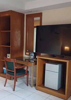 A room with a desk, chair, television, and a small refrigerator. - Bursa Hotel (Patong)