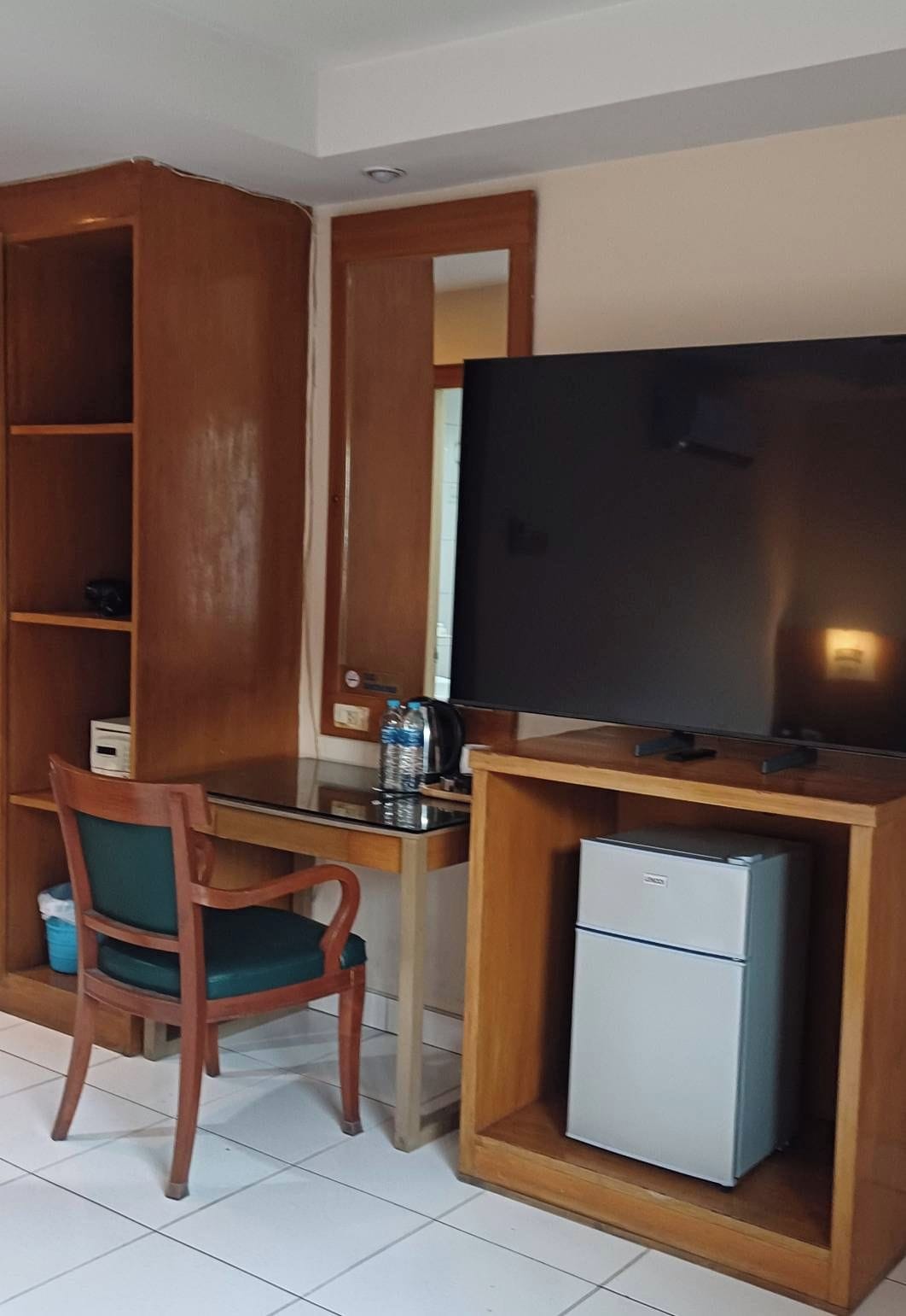 Una habitación compacta con un escritorio de madera, una silla, un televisor y un refrigerador pequeño.