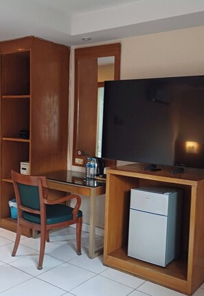 A compact room with a wooden desk, a chair, a television, and a small refrigerator. - Bursa Hotel (Patong)