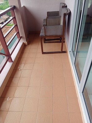 A balcony with a wooden chair, tiled floor, and a glass door. - Bursa Hotel (Patong)