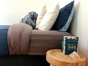 A bedroom with a bed, pillows, a book titled 'Bag of Jewels,' and a small wooden stool.