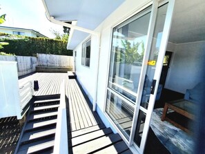 Een overdekt buitengebied met een houten terras, een schuifdeur naar een kamer en een kleine tafel.