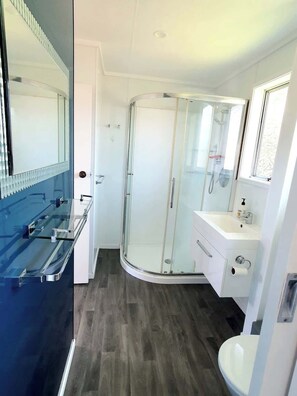 Een moderne badkamer met een douchecabine van glas, een witte wastafel en een grote spiegel.