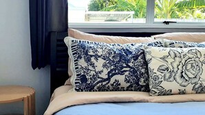 Ein Bett mit blumigem Kissenbezug, ein Nachttisch aus Holz und ein Fenster mit Blick auf Grünflächen.